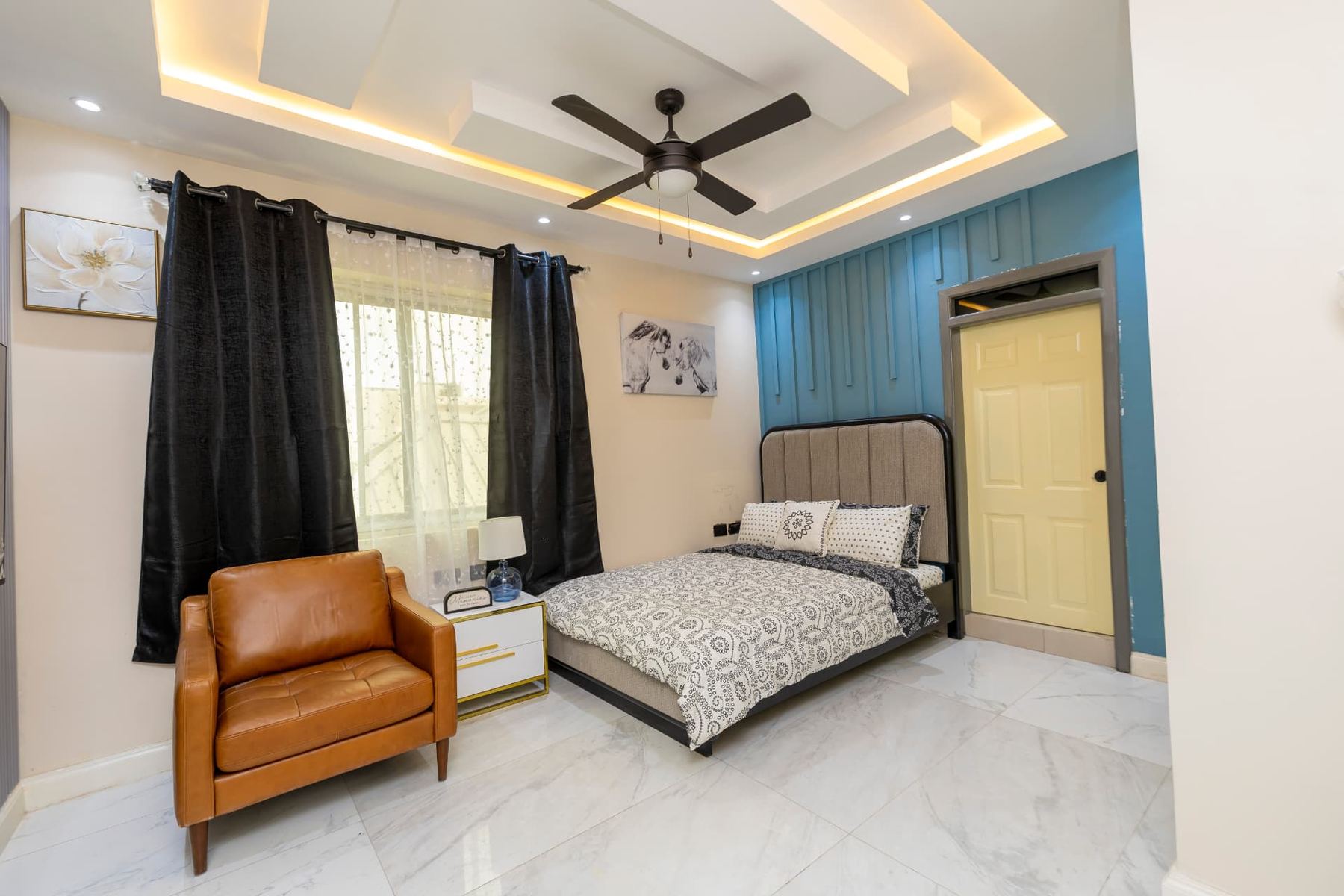 Unit 107 bedroom with queen bed, tan leather armchair, teal panelled wall and ceiling fan