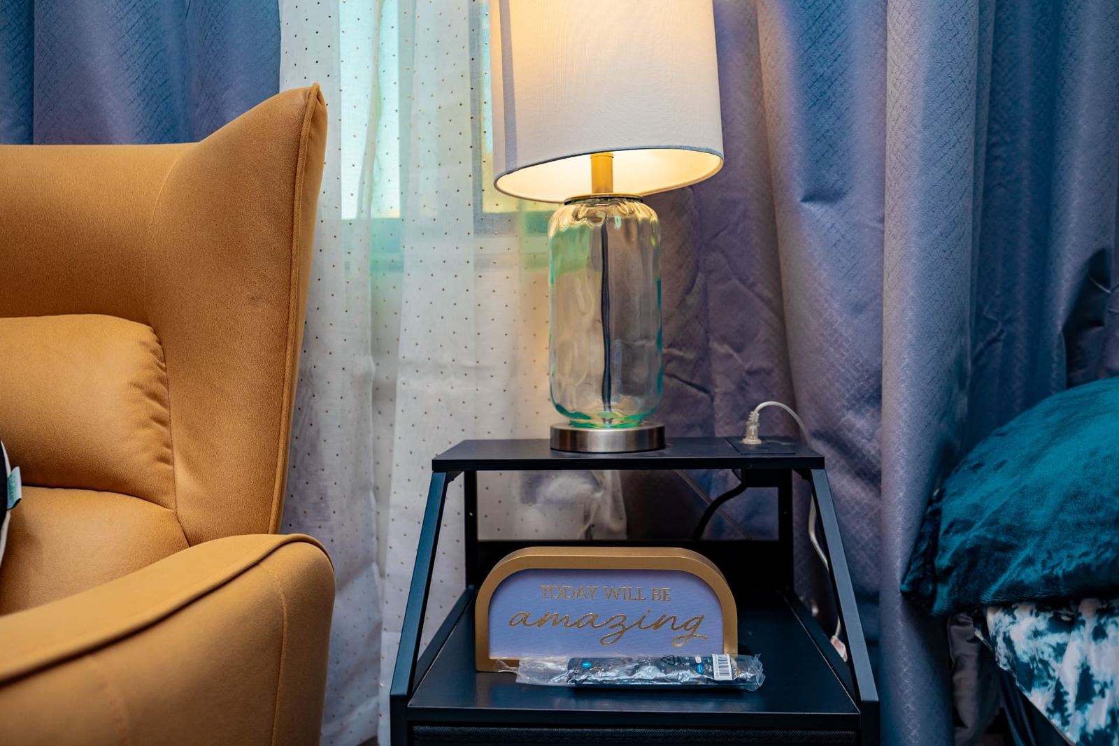 Bedside table with glass lamp beside a mustard reading chair